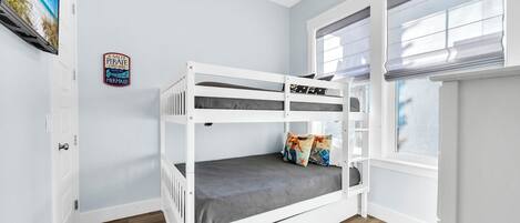 Een stapelbed met een grijze matras, een plafondventilator, een raam met jaloezieën en een wanddecoratie.