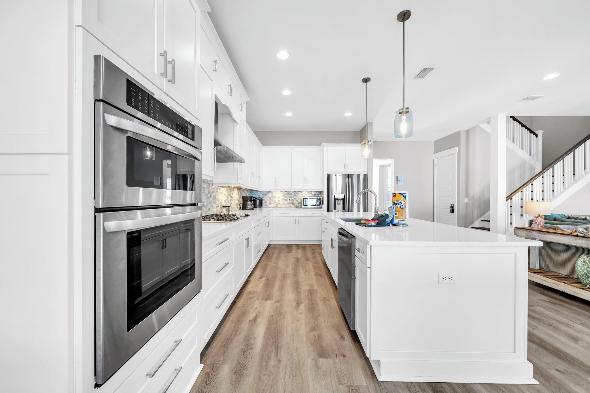 A modern kitchen with white cabinetry, stainless steel appliances, a wooden floor, and a central island.