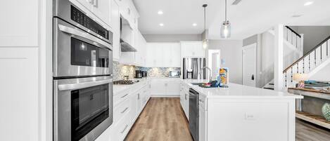 A modern kitchen with white cabinetry, stainless steel appliances, a wooden floor, and a central island.