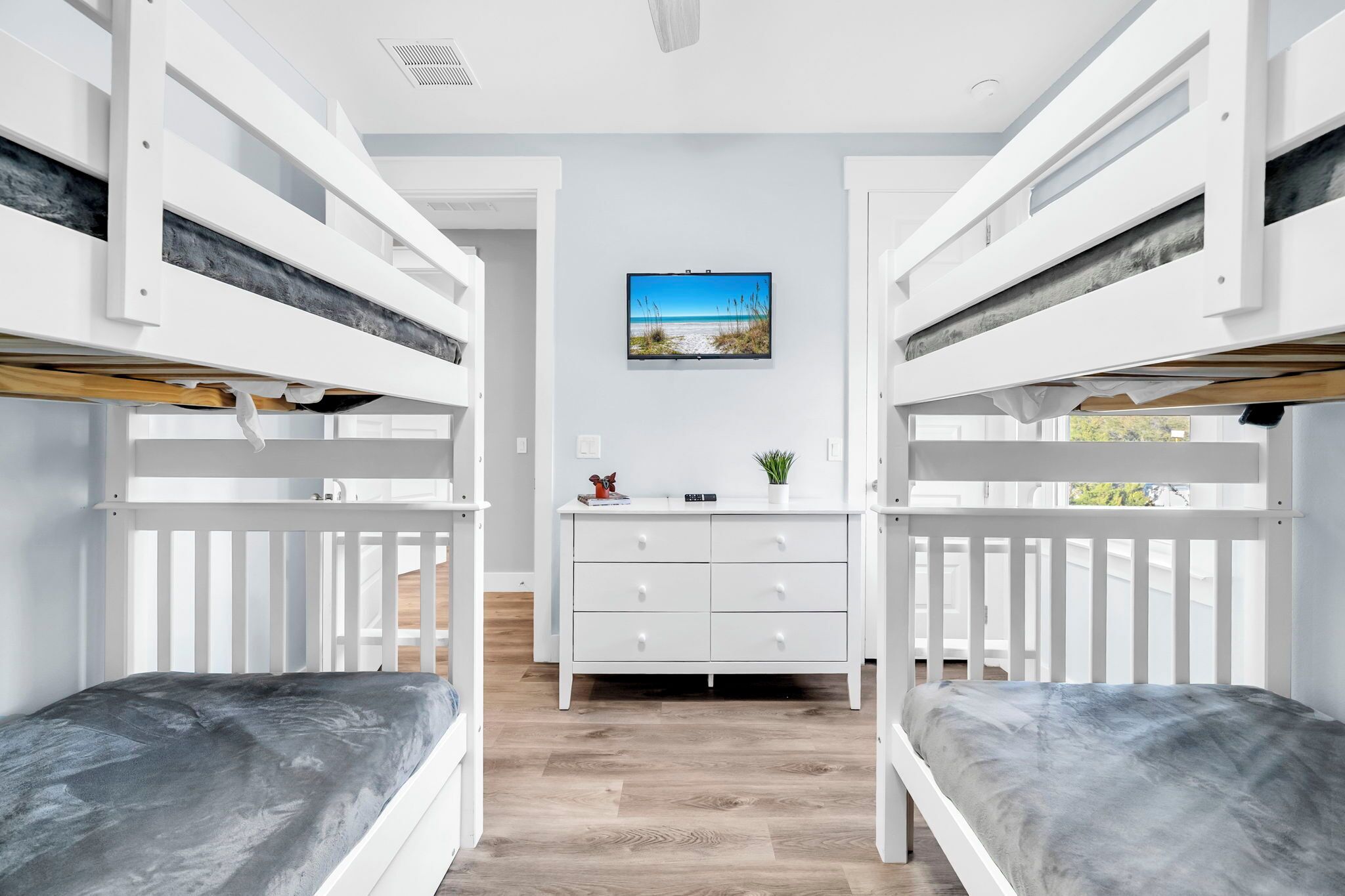 A room with bunk beds, a central white dresser, and a wall-mounted TV.