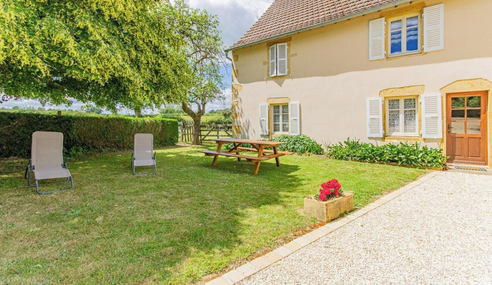 Ein Haus mit befestigter Auffahrt, einem Holztisch und zwei Stühlen im Garten.
