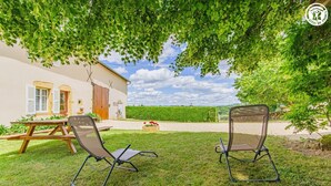 Een terras met twee stoelen, een tafel en een huis met een groot raam en luiken.