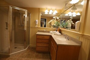 Ein Badezimmer mit einer Glaskabine zur Dusche, einem Waschbecken mit Spiegel darüber und einer Vase mit Blumen.
