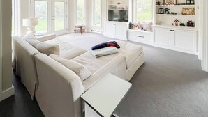 Una habitación amplia con un sofá grande, una mesita, un televisor y una estantería empotrada.
