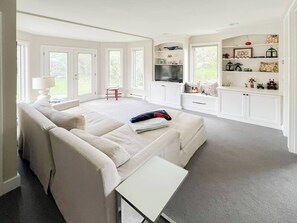 Ein geräumiger Raum mit großem Sofa, kleinem Tisch, Fernseher und einer integrierten Regaleinrichtung.