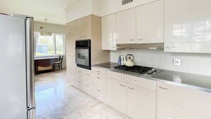 Una cocina moderna con armarios blancos, un refrigerador de acero inoxidable, un horno, una estufa y una tetera.