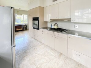 Eine moderne Küche mit weißen Schränken, einem Edelstahl-Kühlschrank, einem Backofen, einem Herd und einem Wasserkocher.
