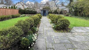 Un sendero de piedra conduce a una casa con puerta azul, rodeada de setos cuidados y una valla de madera.