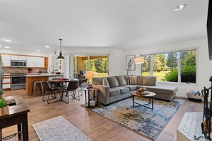 A modern kitchen with a dining area, a sofa, and large windows with a view of greenery. - Arrowleaf | Golf & Pond Views | Ground-Floor Kahler Glen Condo | Sleeps 4 (Leavenworth)