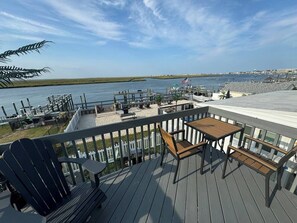 Een terras met tafel en stoelen, met uitzicht op een wateroppervlak en een verre kustlijn.