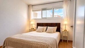 Quarto com uma cama grande, duas mesas de cabeceira, uma janela com cortinas e uma cabeceira de madeira.