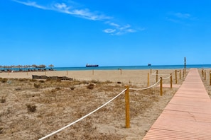 Ein Strand mit einem hölzernen Weg, der zu Strandstühlen und Sonnenschirmen führt.