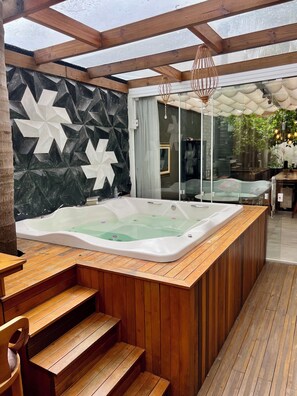 Un jacuzzi en un área exterior cubierta con escalones de madera y un diseño de pared geométrico.