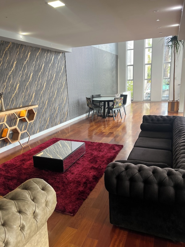 A modern living room with a sofa, a coffee table, a rug, and a dining area with chairs and a table.