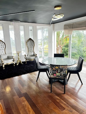 A modern dining area with a glass table, black leather chairs, and a chandelier.