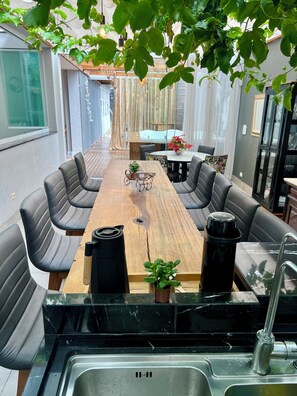 Un comedor moderno con una mesa de madera, sillas de cuero negro, una pequeña planta en maceta y un hervidor eléctrico negro.