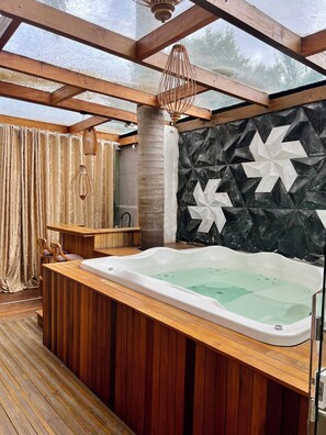 Una terraza de madera con un jacuzzi, mobiliario de madera y un muro decorativo con patrones geométricos.
