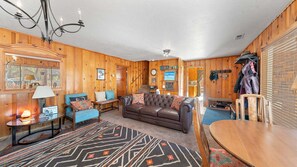 Ein gemütliches Blockhaus-Interieur mit Ledersofa, Esstisch aus Holz und einem gemusterten Teppich.