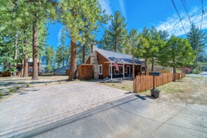 A rustic cabin with a brick exterior, surrounded by tall pine trees, a paved driveway, and a wooden fence. - 1 Block from Regan Beach | BBQ | Deck (South Lake Tahoe)