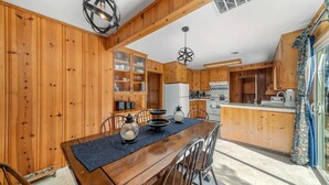 A wooden interior with a dining table, chairs, a refrigerator, and a kitchen area. - Regan Beach Retreat Cabin | CYH0809 (South Lake Tahoe)