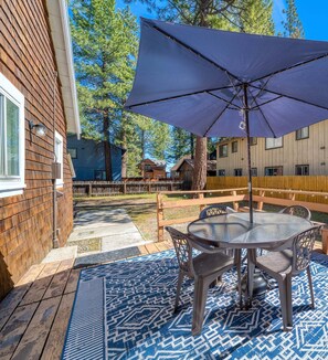 Eine Terrasse mit einem runden Tisch, Stühlen, einem violetten Sonnenschirm und einem gemusterten Teppich.