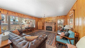 A cozy cabin interior with a fireplace, leather sofa, and a dining area. - Regan Beach Retreat Cabin | CYH0809 (South Lake Tahoe)