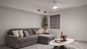 Un saló modern amb un sofà modular, una taula de centre rodona, un ventilador de sostre i una planta en test.