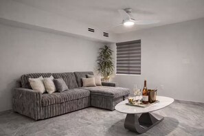 Ein modernes Wohnzimmer mit einem Ecksofa, einem runden Couchtisch, einem Deckenventilator und einer Topfpflanze.