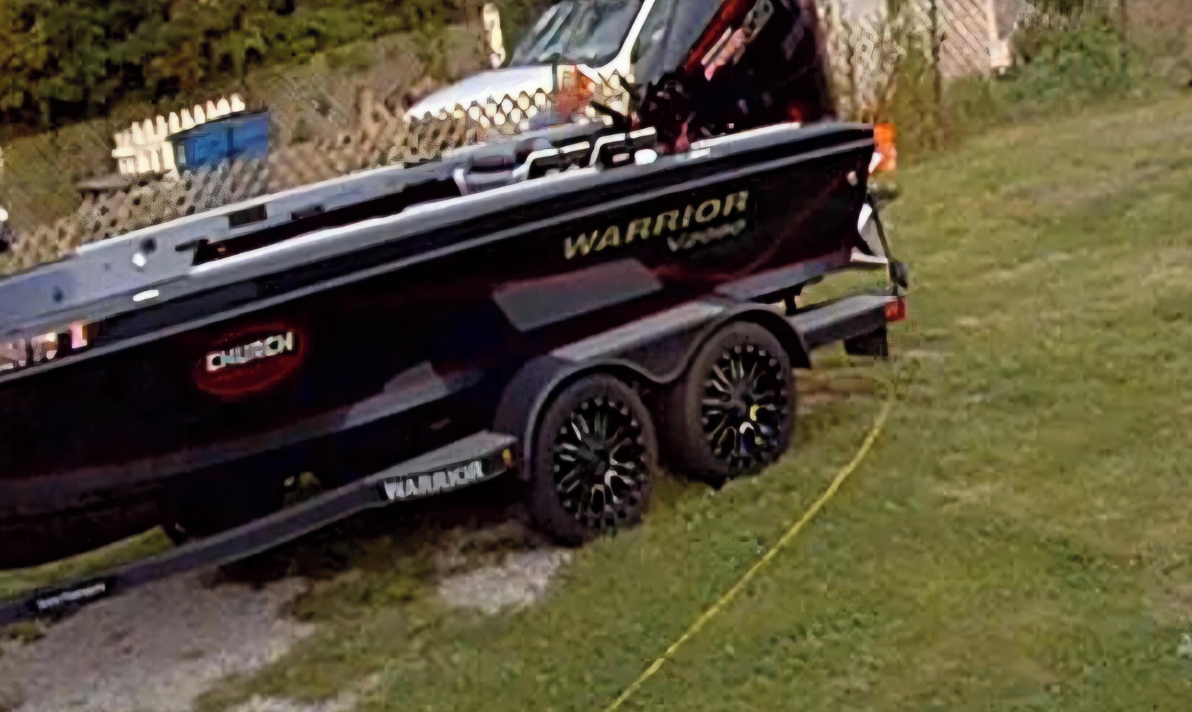 A black boat with 'WARRIOR' written on the side, parked on grass.