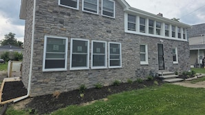 A two-story stone house with multiple windows, a front door, and a small front yard with a garden bed. - Lake Erie Fishing - Sleeps 8 · 3 Bd - 1.5 Bth - Full Kitchen - Patio - Out Elec. (Lorain)