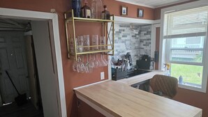 A kitchen with a wooden countertop, a sink, a window with blinds, and a shelf with glassware. - Lake Erie Fishing - Sleeps 8 · 3 Bd - 1.5 Bth - Full Kitchen - Patio - Out Elec. (Lorain)