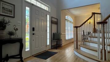 A spacious foyer with a wooden staircase, a door with a window, and a chair.