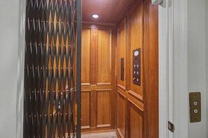Un ascenseur avec un intérieur en bois, une porte de sécurité en métal et un panneau de commande doté de boutons.