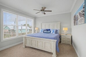 Une chambre à coucher avec un lit, un ventilateur de plafond, une table de chevet avec une lampe et une fenêtre avec des stores.