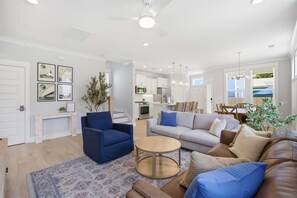 Un salon moderne avec un canapé, des fauteuils, une table basse et, au fond, un coin repas.
