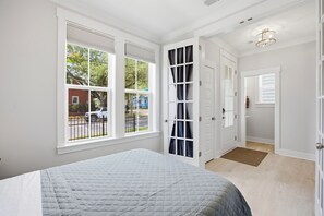 Ein Schlafzimmer mit Bett, großen Fenstern, einer Tür und einer Deckenleuchte.