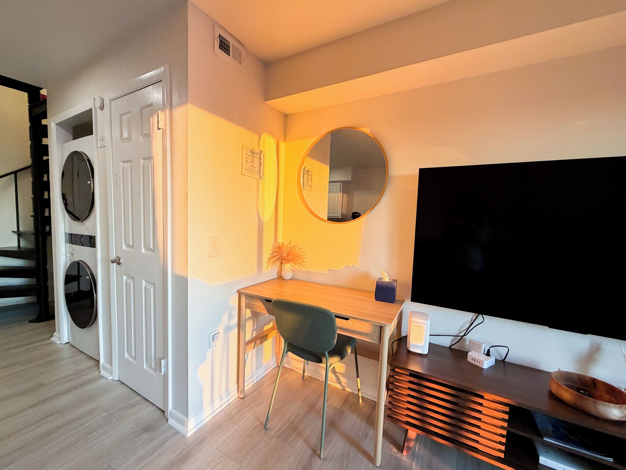 Een knus woongedeelte met een wasmachine, een eethoek met een stoel, een tafel en een grote flatscreen-tv.