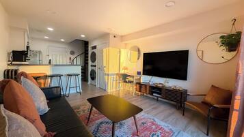 Ein modernes Wohnzimmer mit Sofa, Couchtisch, Fernseher und einer Küche im Hintergrund.