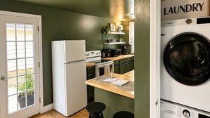 Eine kompakte Küche mit Kühlschrank, Herd und Mikrowelle, eine kleine Bar mit Barhocker und ein Waschbereich mit Waschmaschine.