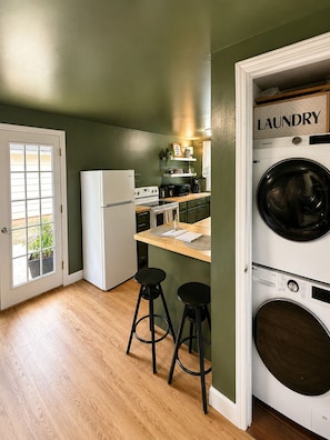 A compact kitchen with a refrigerator, stove, and microwave, a small bar area with stools, and a laundry area with a washing machine.