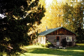 Une cabane rustique en rondins de bois, dotée d’une porte d’entrée, d’une cheminée et d’un petit porche.