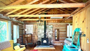 Interior de una cabaña de troncos con piso de madera, un sofá, una mesa, una chimenea y un espejo.