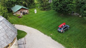 Une cabane en rondins avec un toit végétalisé, une allée en gravier et une voiture sur laquelle est posé un kayak rouge, sur la pelouse.