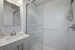 A modern bathroom with a glass-enclosed shower, a white-tiled wall, a marble sink, and a mirror above the sink. - B200 - Azure Shores - North Coast Village (Oceanside)