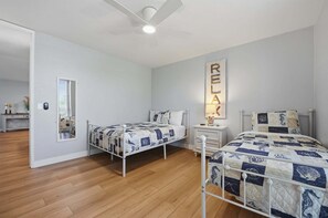 A bedroom with two beds, a ceiling fan, a bedside table, a mirror, and a wall-mounted light.