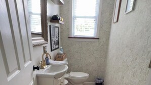 Ein schmales Badezimmer mit einem weißen Waschbecken, einer Toilette und einem Fenster.