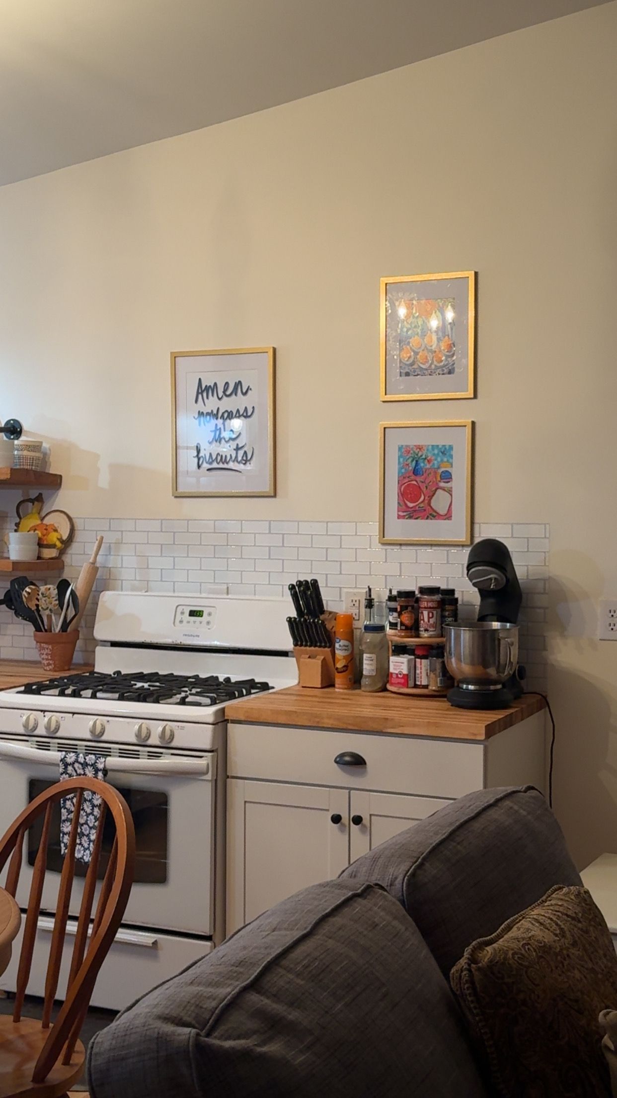 A kitchen with a stove, oven, and various kitchen items on the counter. There are two framed pictures on the wall.