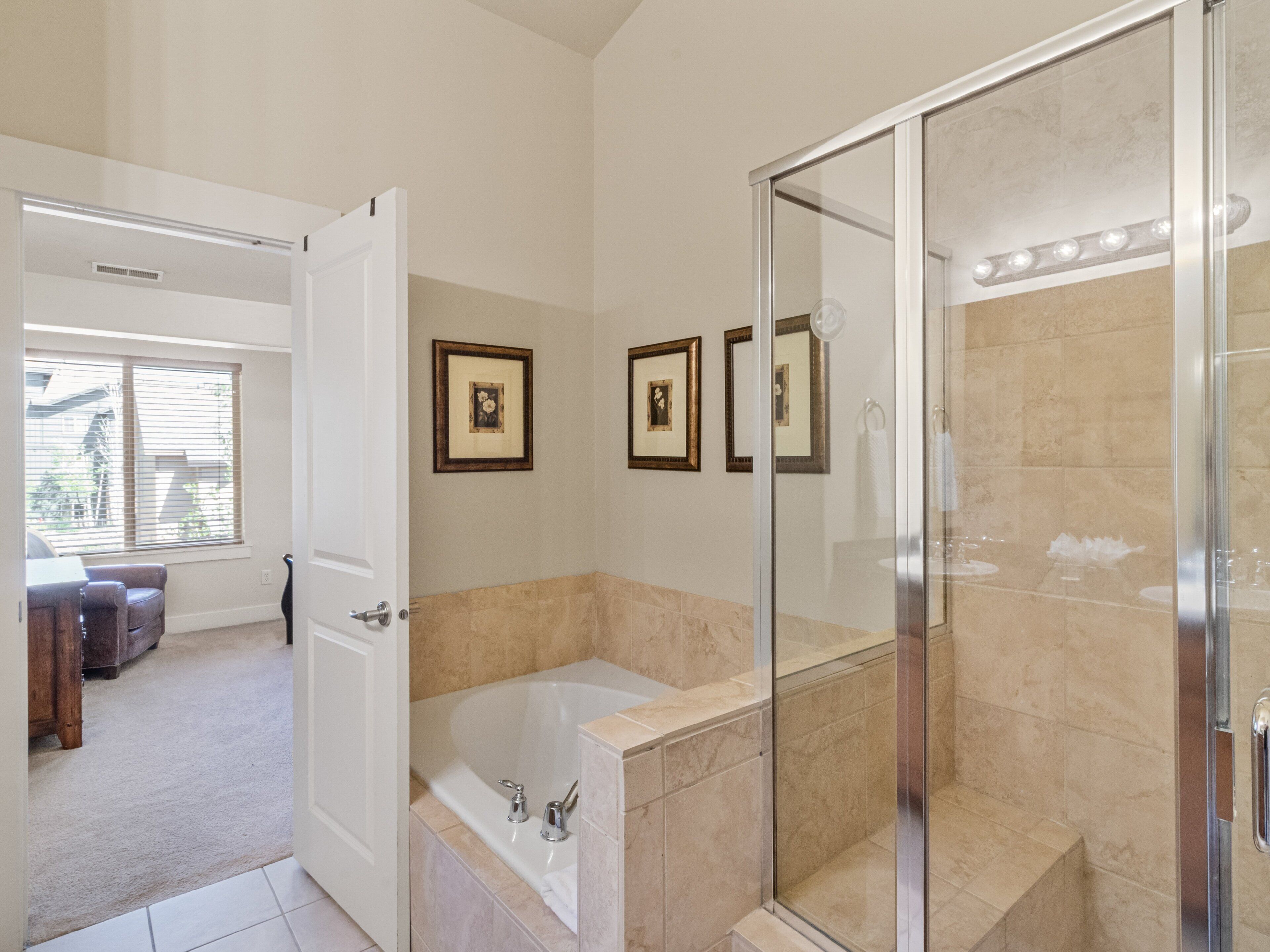 A bathroom with a glass-enclosed shower, a bathtub, and a toilet. There are framed pictures on the wall.