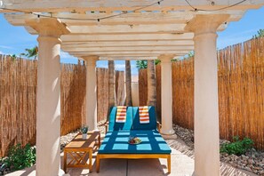 A covered outdoor seating area with a table and chairs, a pergola overhead, and bamboo fencing. - Group Getaway: Heated Pool | Theater | Game Room (Las Vegas)