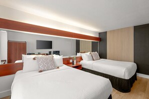 Quarto de hotel com duas camas, um espelho grande, uma TV de tela plana e uma cabeceira de madeira.